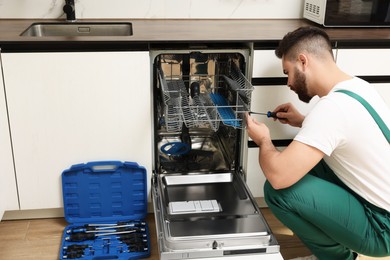 Serviceman repairing dishwasher with screwdriver in kitchen