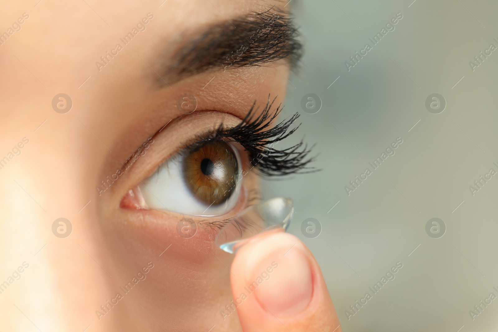 Photo of Woman putting contact lens in her eye on blurred background, closeup