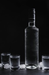 Photo of Bottlevodka and shot glasses with ice on table against black background