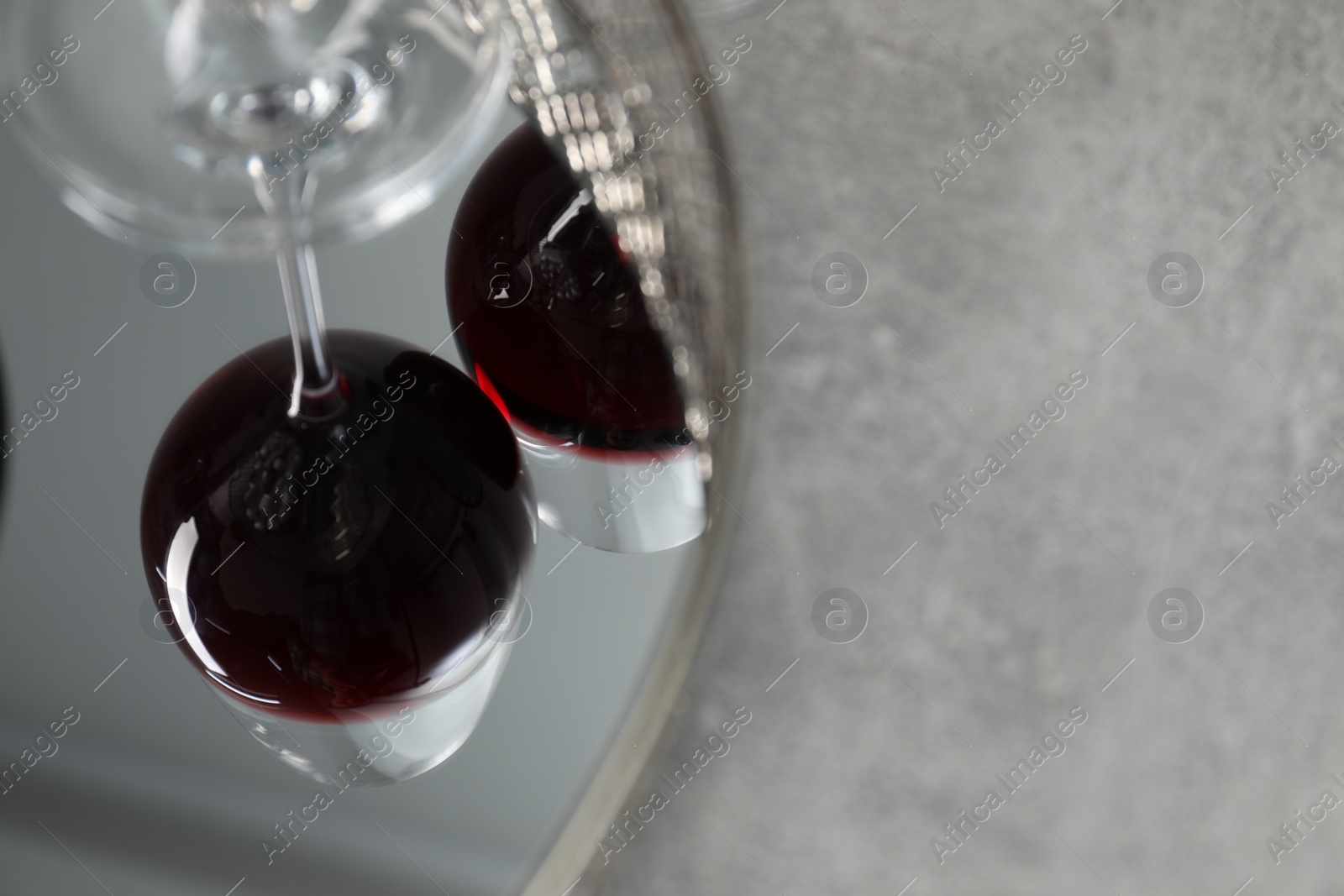 Photo of Mirror tray reflecting glasses of red wine on grey table, closeup