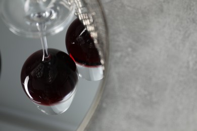 Mirror tray reflecting glasses of red wine on grey table, closeup