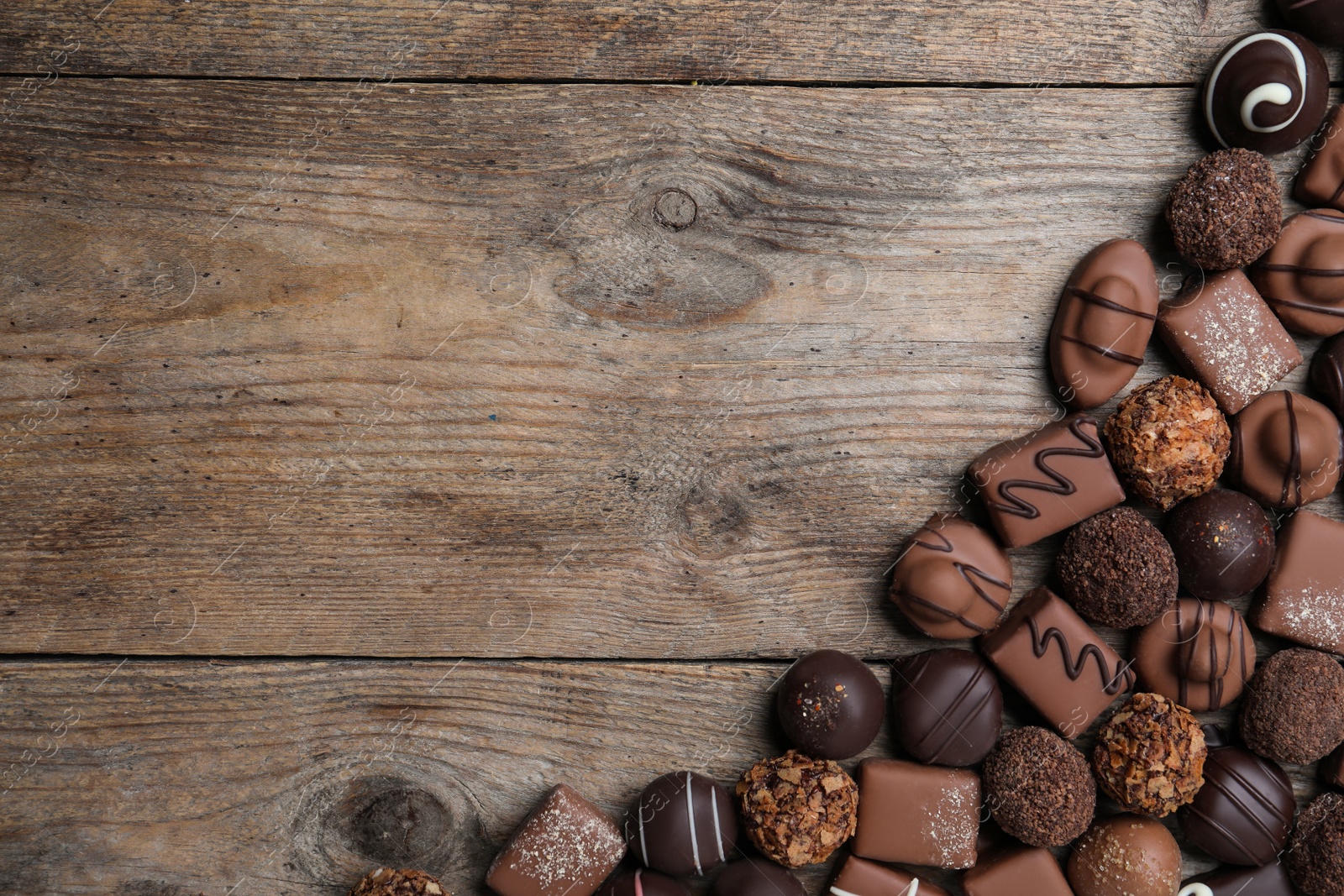 Photo of Different delicious chocolate candies on wooden table, flat lay. Space for text