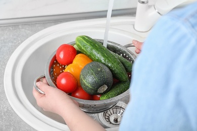 Photo of Woman washing fresh vegetables in colander under water, closeup