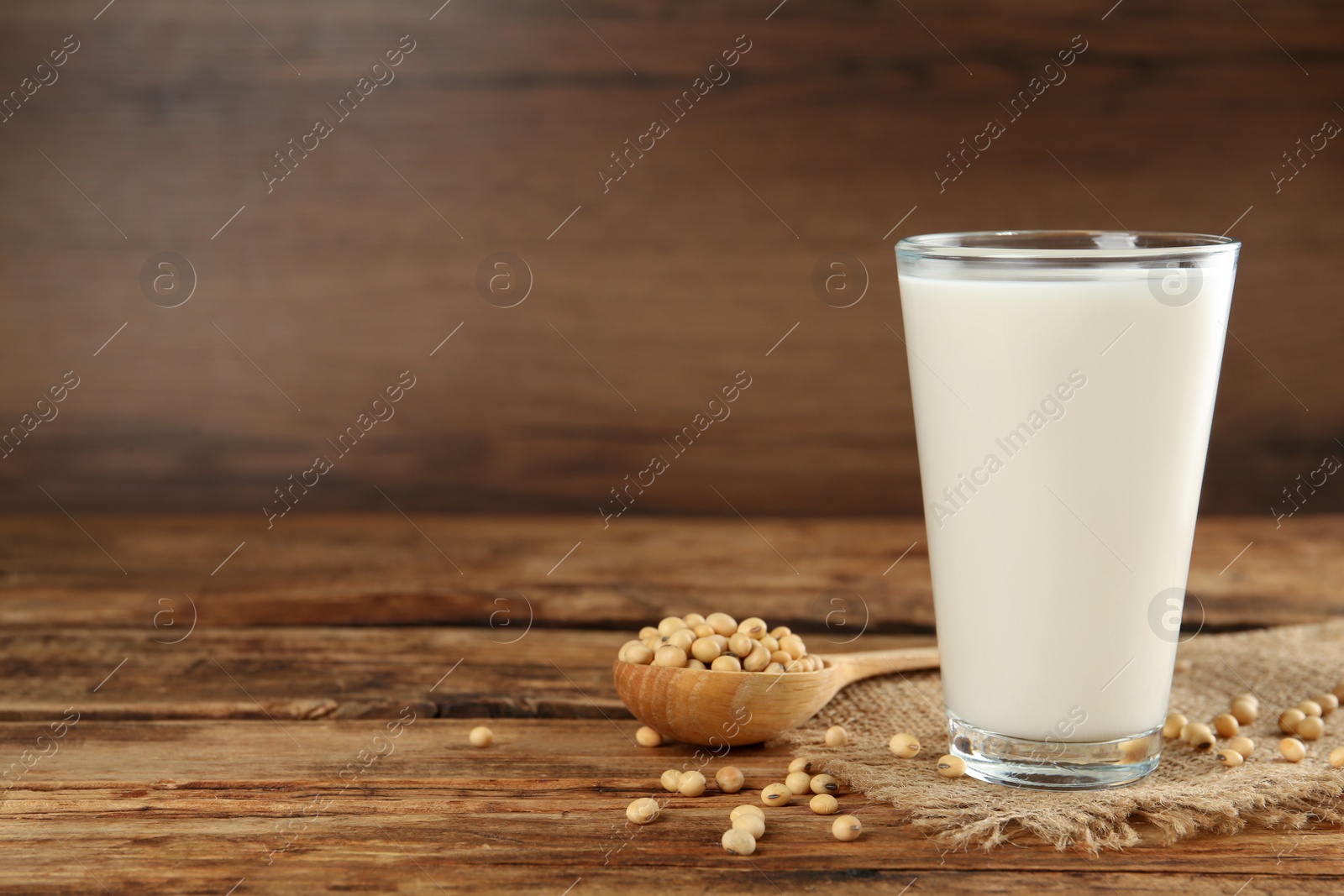 Photo of Glass with fresh soy milk and grains on wooden table. Space for text