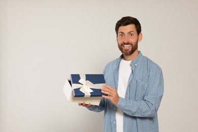 Photo of Emotional man opening gift box on light grey background, space for text
