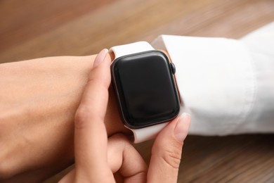Image of Woman checking stylish smart watch at wooden table, closeup