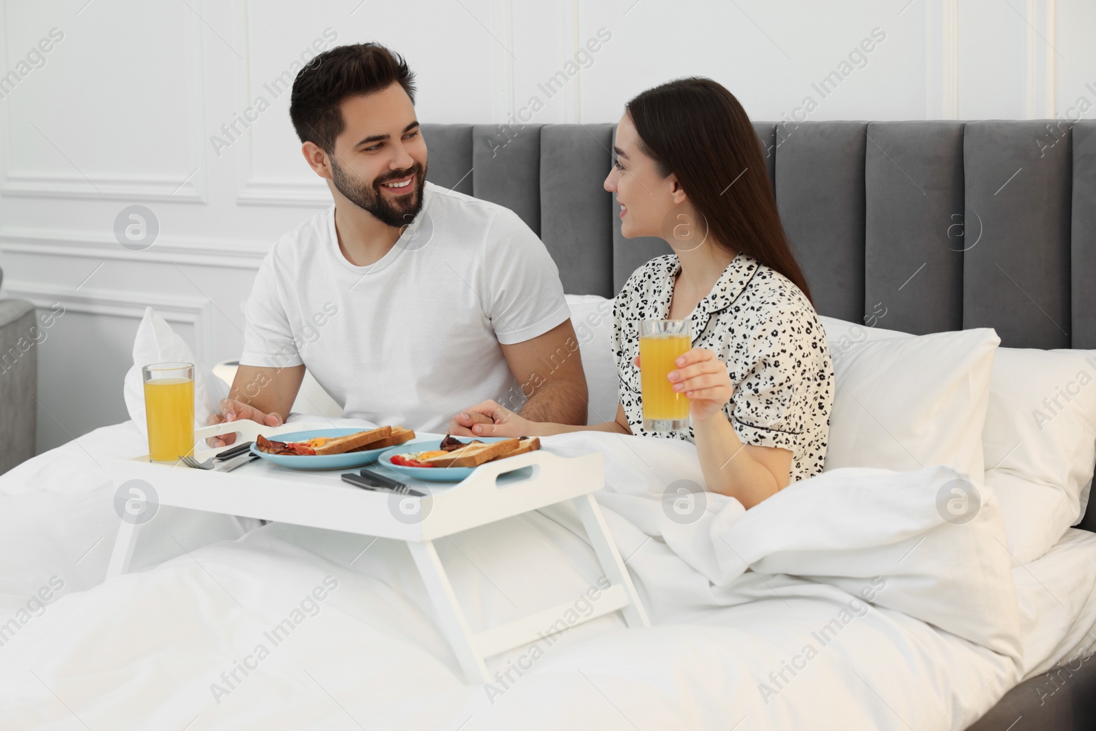 Photo of Happy couple having breakfast on bed at home