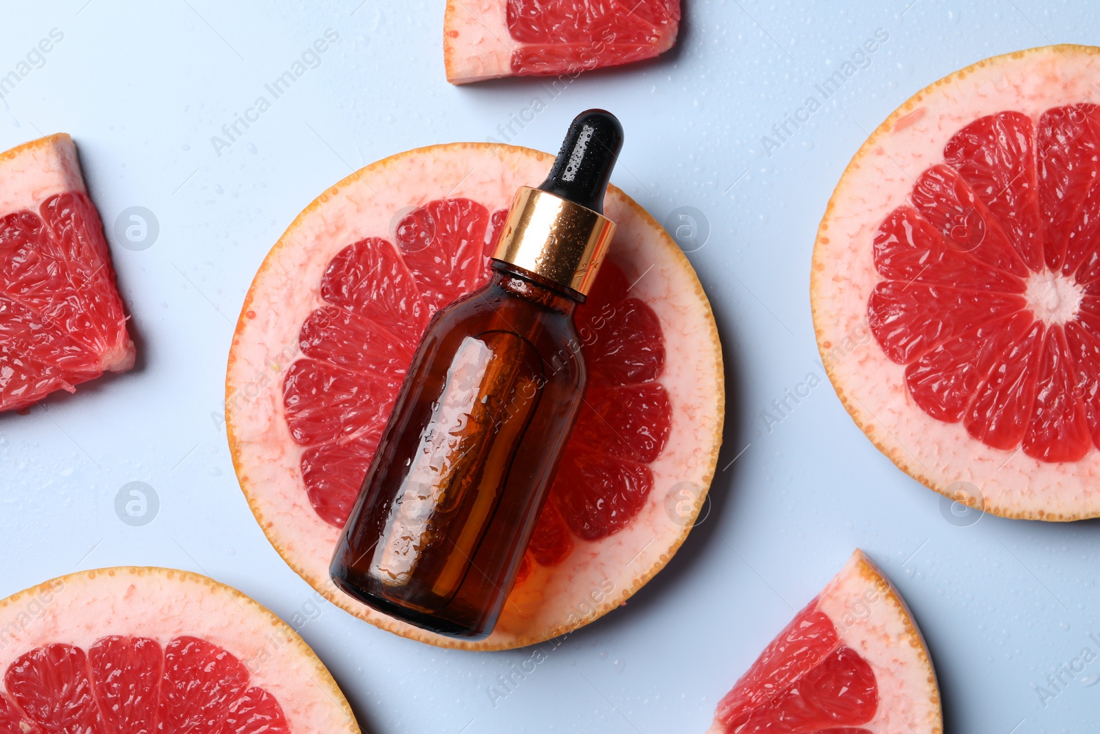 Photo of Bottle of cosmetic serum and grapefruit slices on light blue background, flat lay