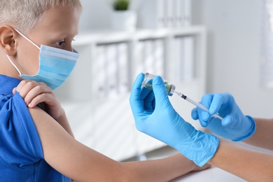 Doctor filling syringe with vaccine for little boy in hospital