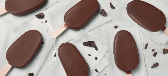 Glazed ice cream bars and chocolate chunks on light grey table, flat lay. Banner design