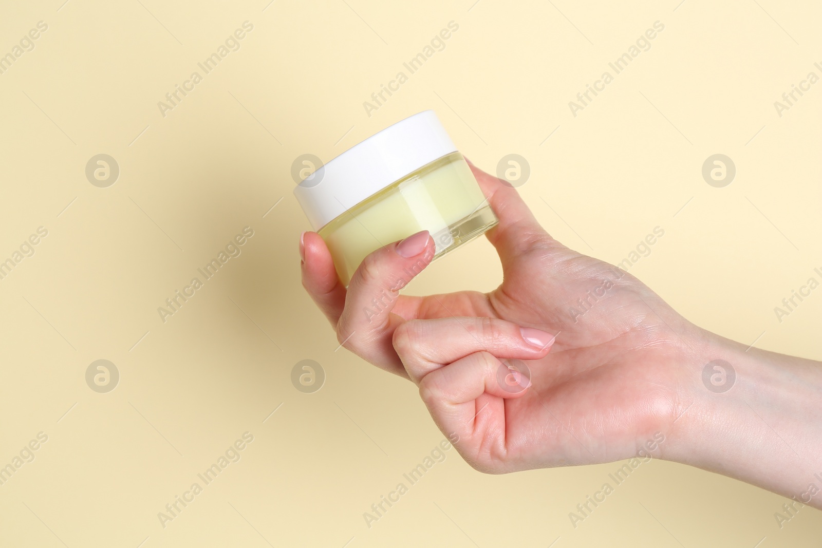 Photo of Woman holding jar of cream on yellow background, closeup