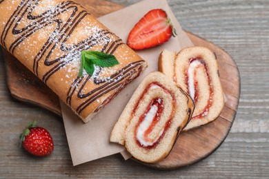 Tasty cake roll with strawberry jam and cream on wooden table, flat lay