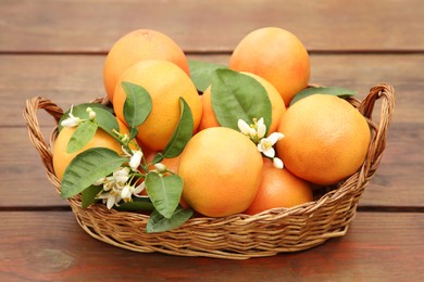 Photo of Wicker basket with fresh grapefruits and green leaves on wooden table
