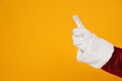 Photo of Santa Claus pointing at something on yellow background, closeup of hand. Space for text