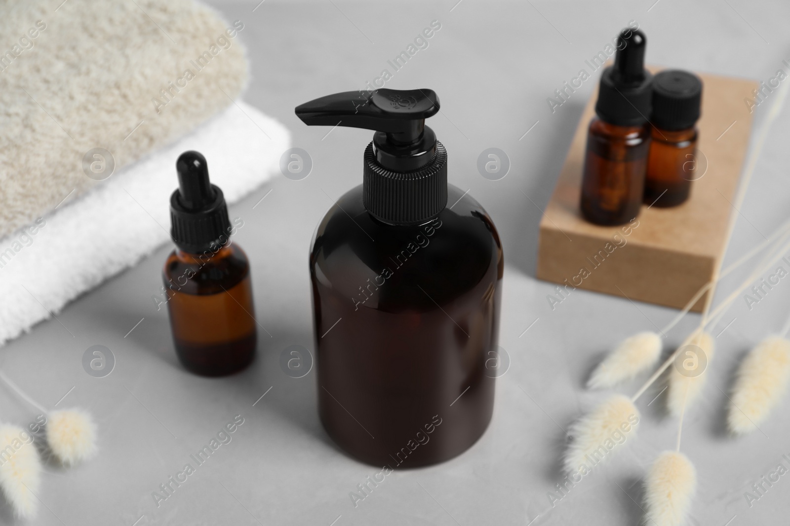 Photo of Bottles with different cosmetic products, dry decorative spikes and soft towels on light grey table, closeup