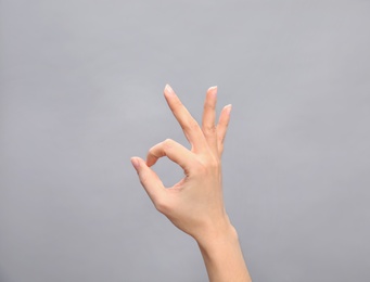 Woman showing sign okay on grey background, closeup. Body language