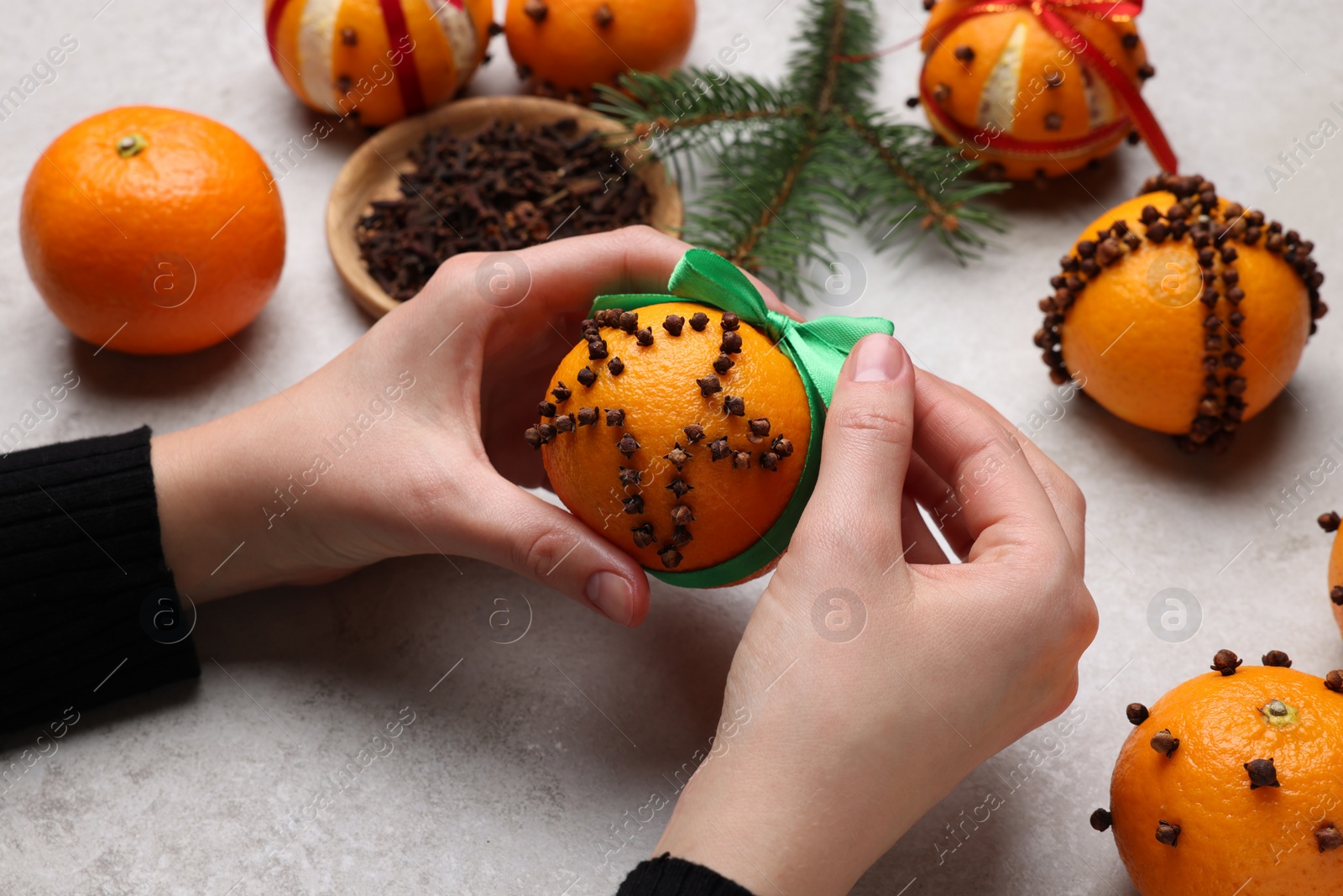 Photo of Woman holding pomander ball with green ribbon made of fresh tangerine and cloves at grey table, closeup