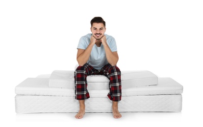 Young man sitting on mattress pile against white background