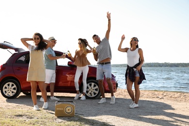 Happy friends having fun near car on beach. Summer trip