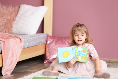 Photo of Cute little girl in princess dress reading book at home