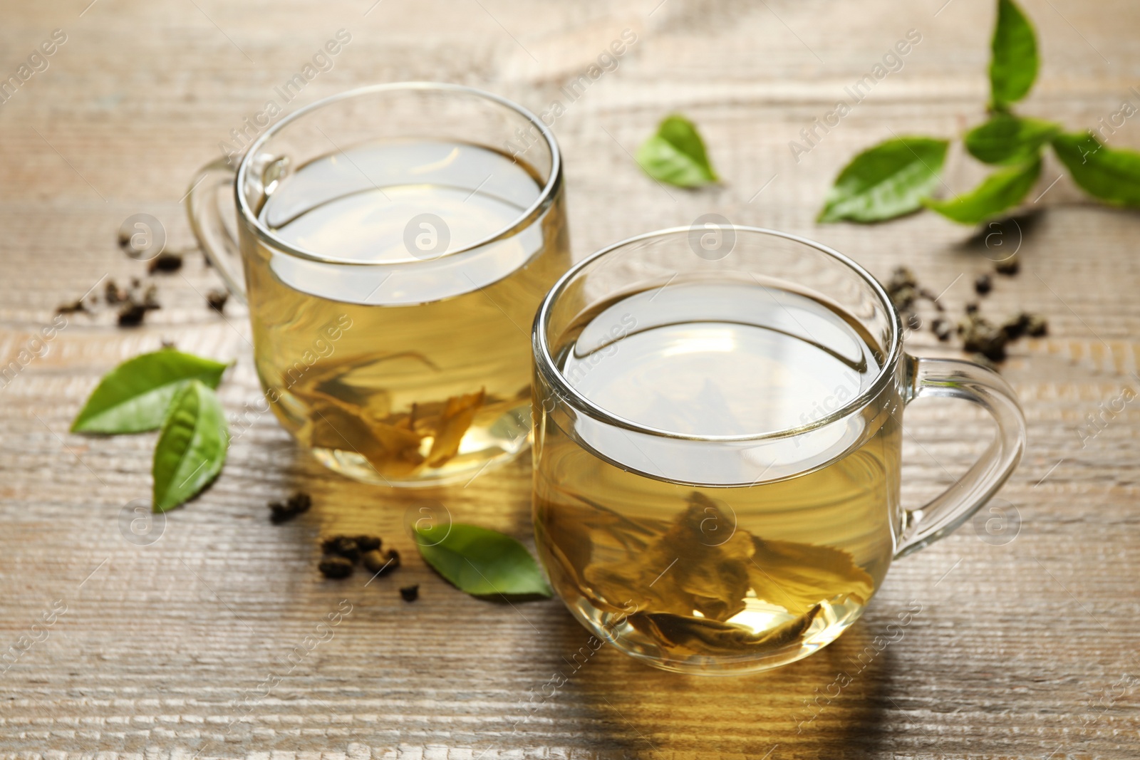 Photo of Cups of green tea, dry and fresh leaves on wooden table