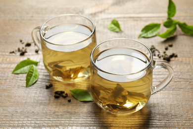 Photo of Cups of green tea, dry and fresh leaves on wooden table