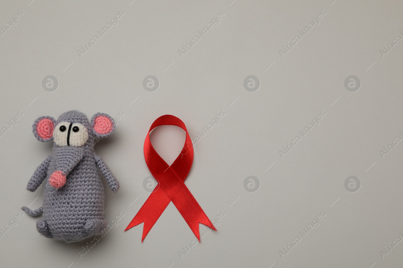 Photo of Cute knitted toy mouse and red ribbon on beige background, flat lay with space for text. AIDS disease awareness