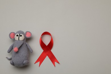 Cute knitted toy mouse and red ribbon on beige background, flat lay with space for text. AIDS disease awareness