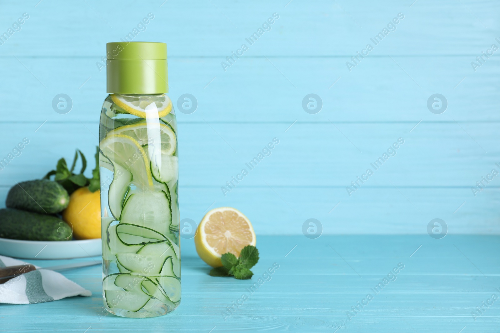 Photo of Bottle of refreshing water with cucumber, lemon and mint on light blue wooden table, space for text