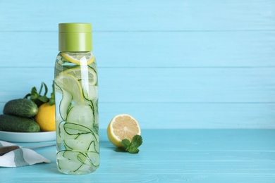 Bottle of refreshing water with cucumber, lemon and mint on light blue wooden table, space for text