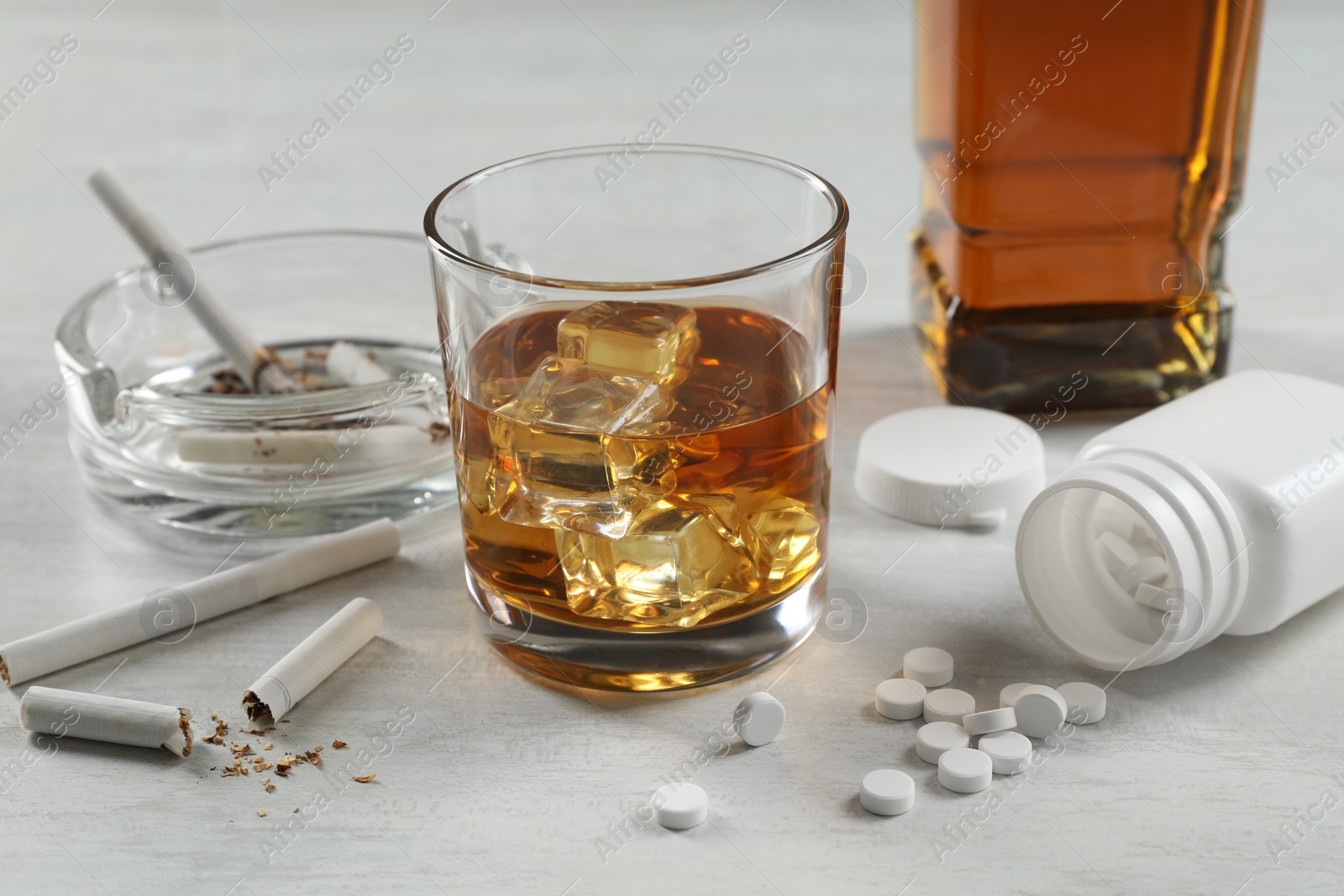 Photo of Alcohol and drug addiction. Whiskey in glass, cigarettes and pills on white table