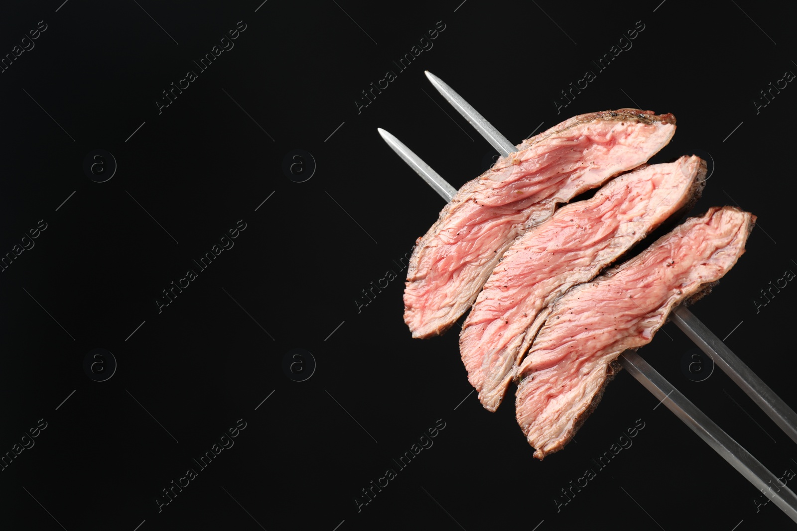 Photo of Meat fork with grilled beef pieces on black background, closeup. Space for text