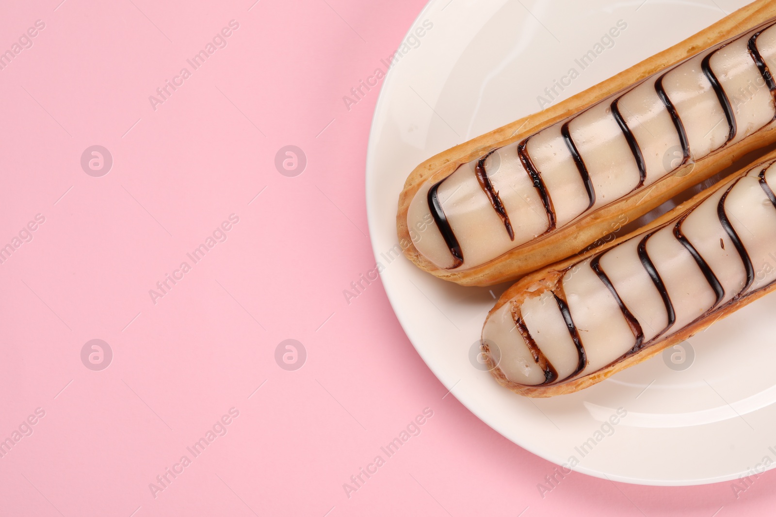 Photo of Delicious eclairs covered with glaze on pink background, top view. Space for text