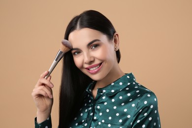 Photo of Beautiful woman applying makeup on light brown background