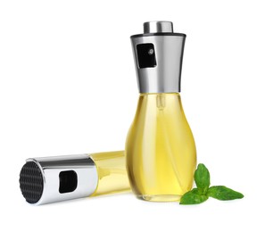 Spray bottles of cooking oil and basil leaves on white background