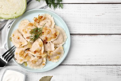 Photo of Cooked dumplings (varenyky) with tasty filling, fried onions and dill on wooden table, flat lay. Space for text