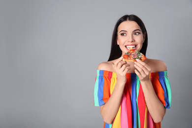 Beautiful woman eating pizza on grey background, space for text