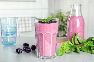 Glass of tasty blackberry smoothie and ingredients on light grey table