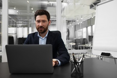 Photo of Man working on laptop at black desk in office. Space for text