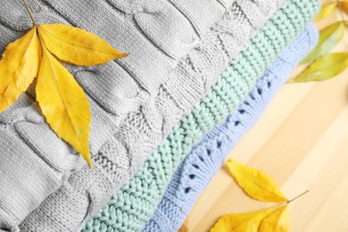 Photo of Stack of warm clothes and autumn leaves on wooden background, above view