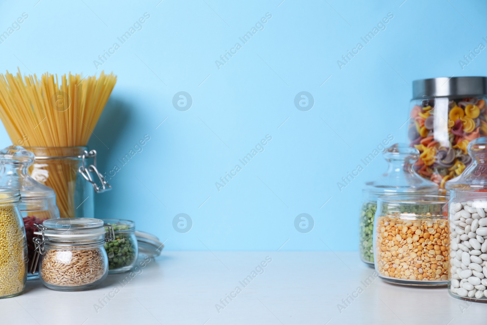 Photo of Glass jars with different types of groats and pasta on white wooden table