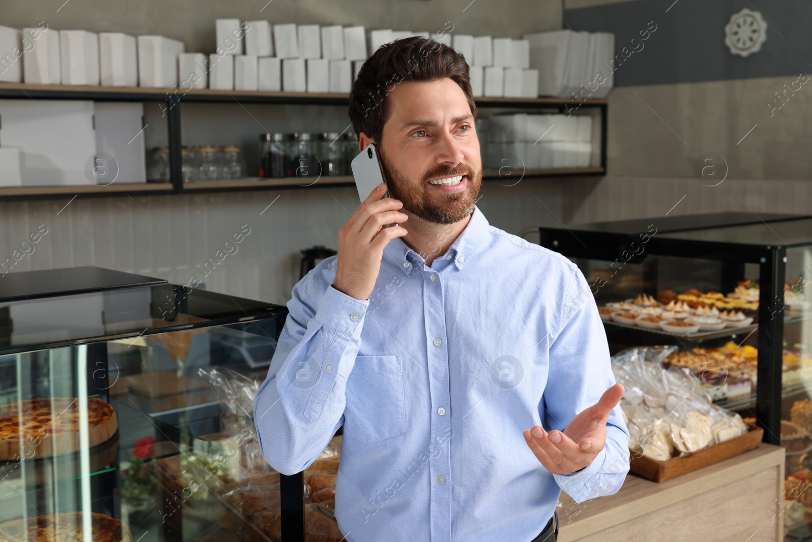 Photo of Happy business owner talking on phone in bakery shop