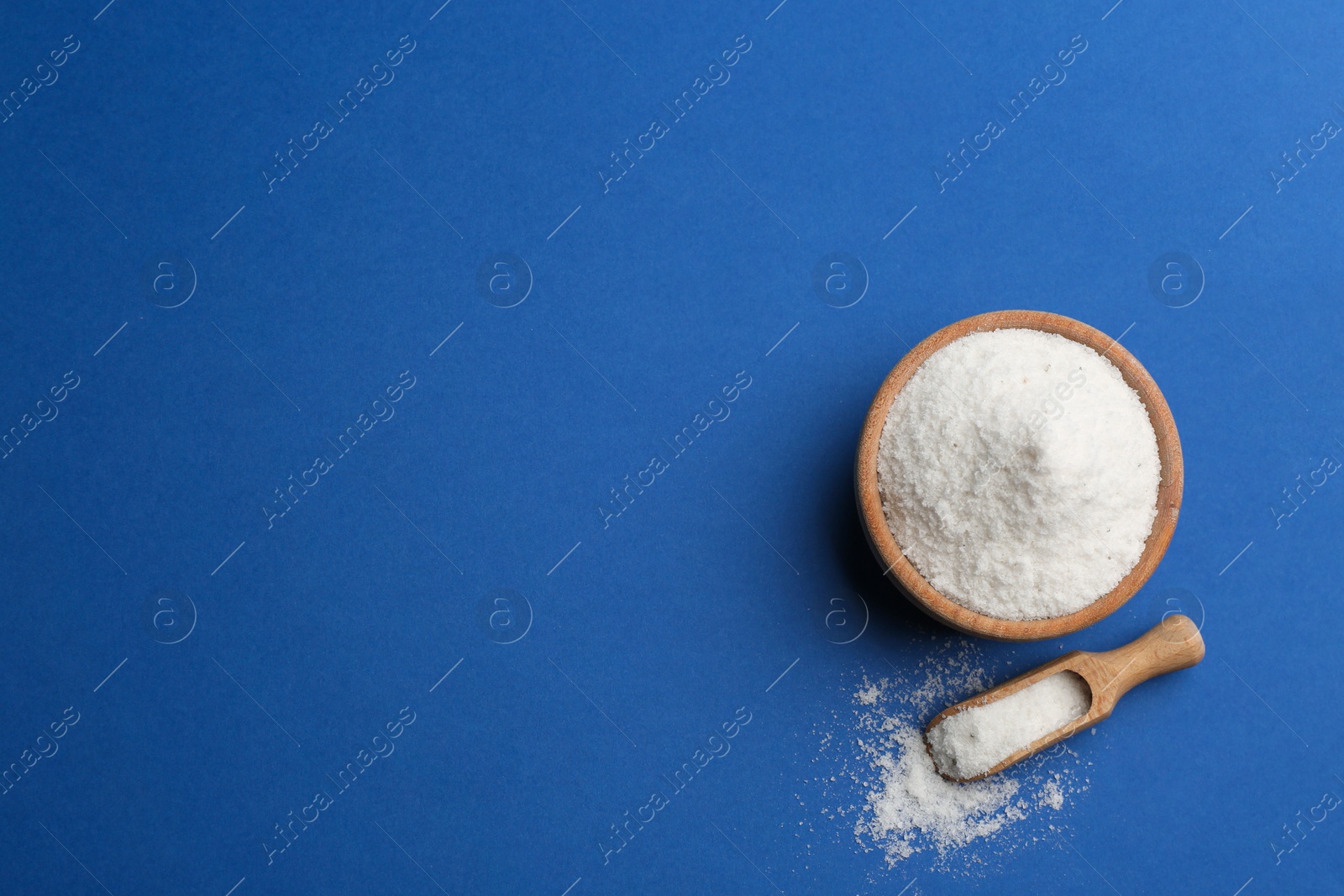 Photo of Bowl and scoop with salt on blue background, flat lay. Space for text