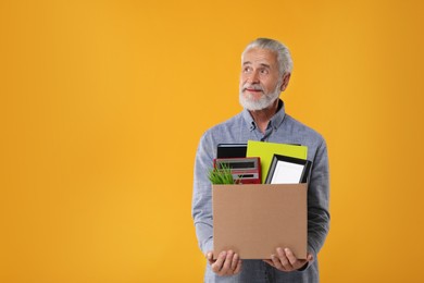 Photo of Happy unemployed senior man with box of personal office belongings on orange background. Space for text