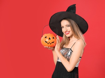 Photo of Beautiful woman wearing witch costume with Jack O'Lantern candy container on red background, space for text. Halloween party