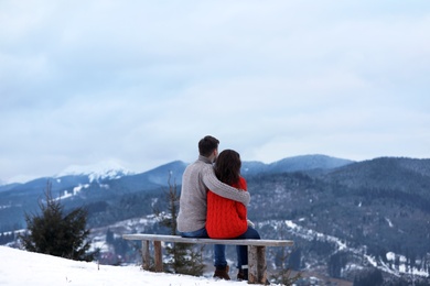 Photo of Couple sitting on bench and enjoying mountain landscape. Winter vacation