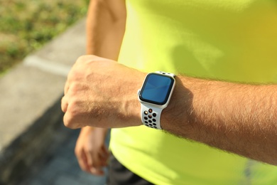 Photo of Man checking modern smart watch during training outdoors, closeup