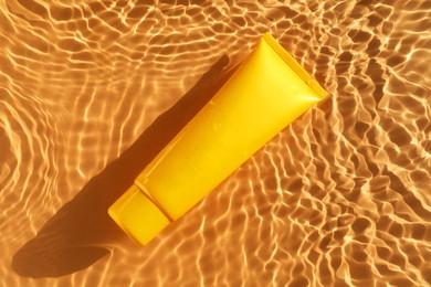 Photo of Tube with moisturizing cream in water on orange background, top view