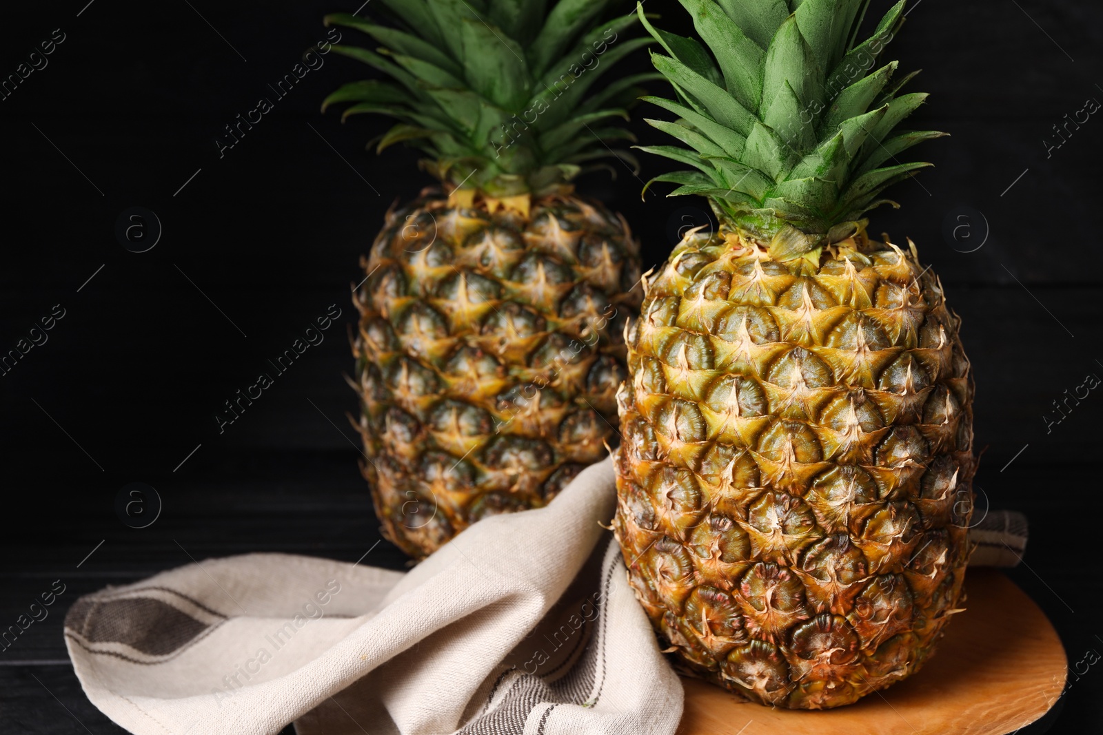 Photo of Whole ripe pineapples on black wooden table. Space for text