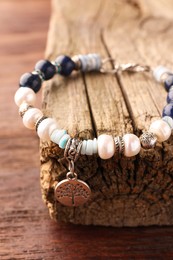 Photo of Beautiful bracelet with gemstones and decorative piece of wood on table, closeup